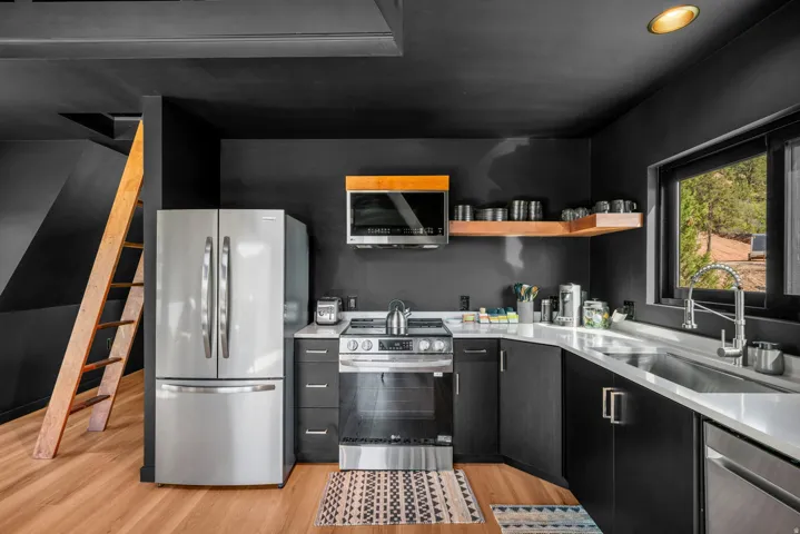 Kitchen with dark cabinets, stainless steel appliances, light wood-style flooring, exhaust hood, and open shelves