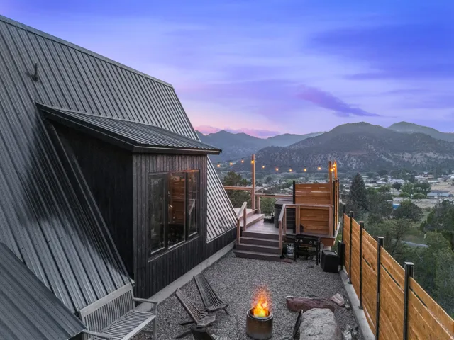 Property exterior at dusk with a deck with mountain view, an outdoor fire pit, a fenced backyard, and a metal roof