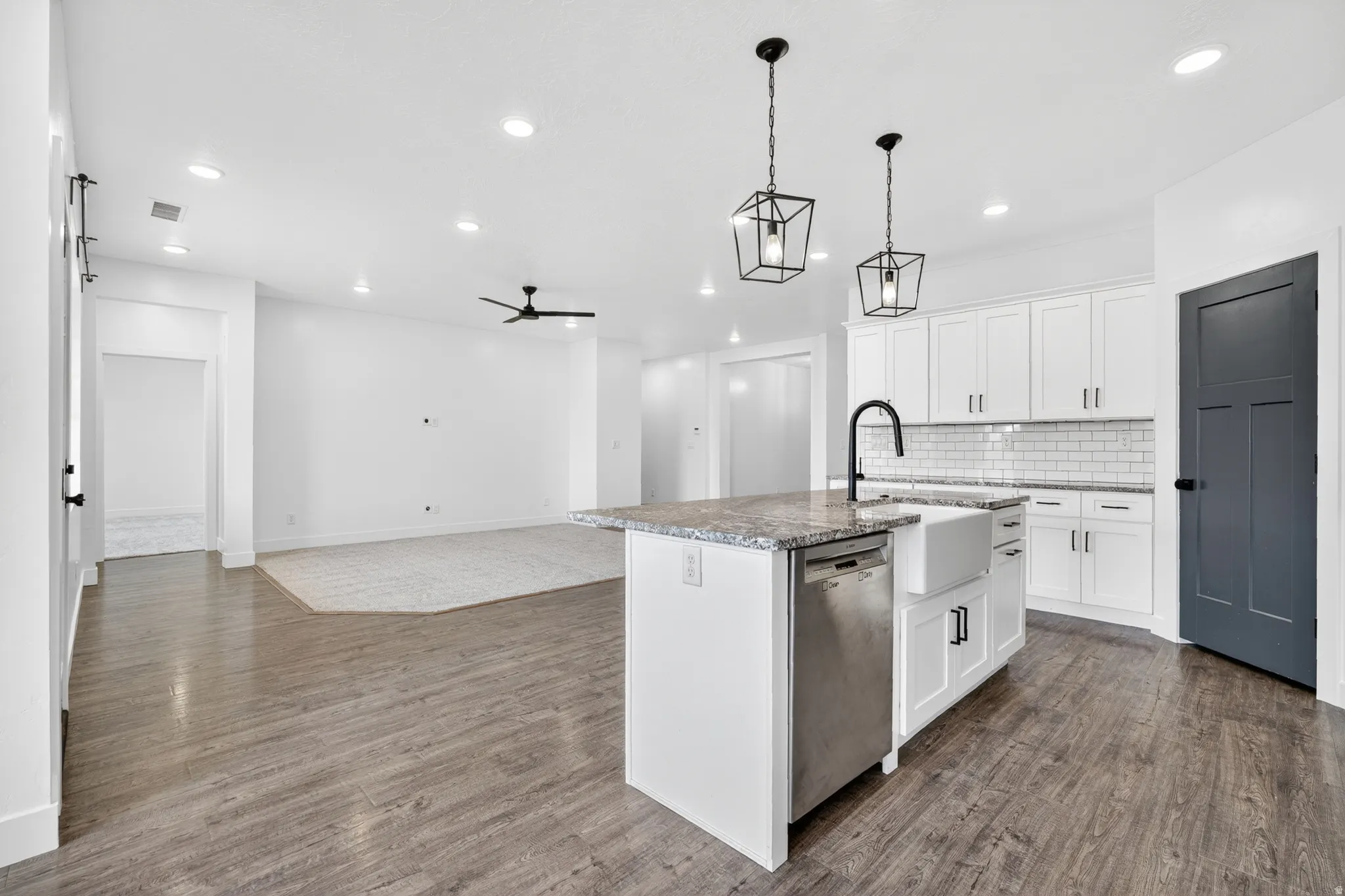 Kitchen featuring white cabinets, a ceiling fan, an island with sink, dishwasher, and backsplash