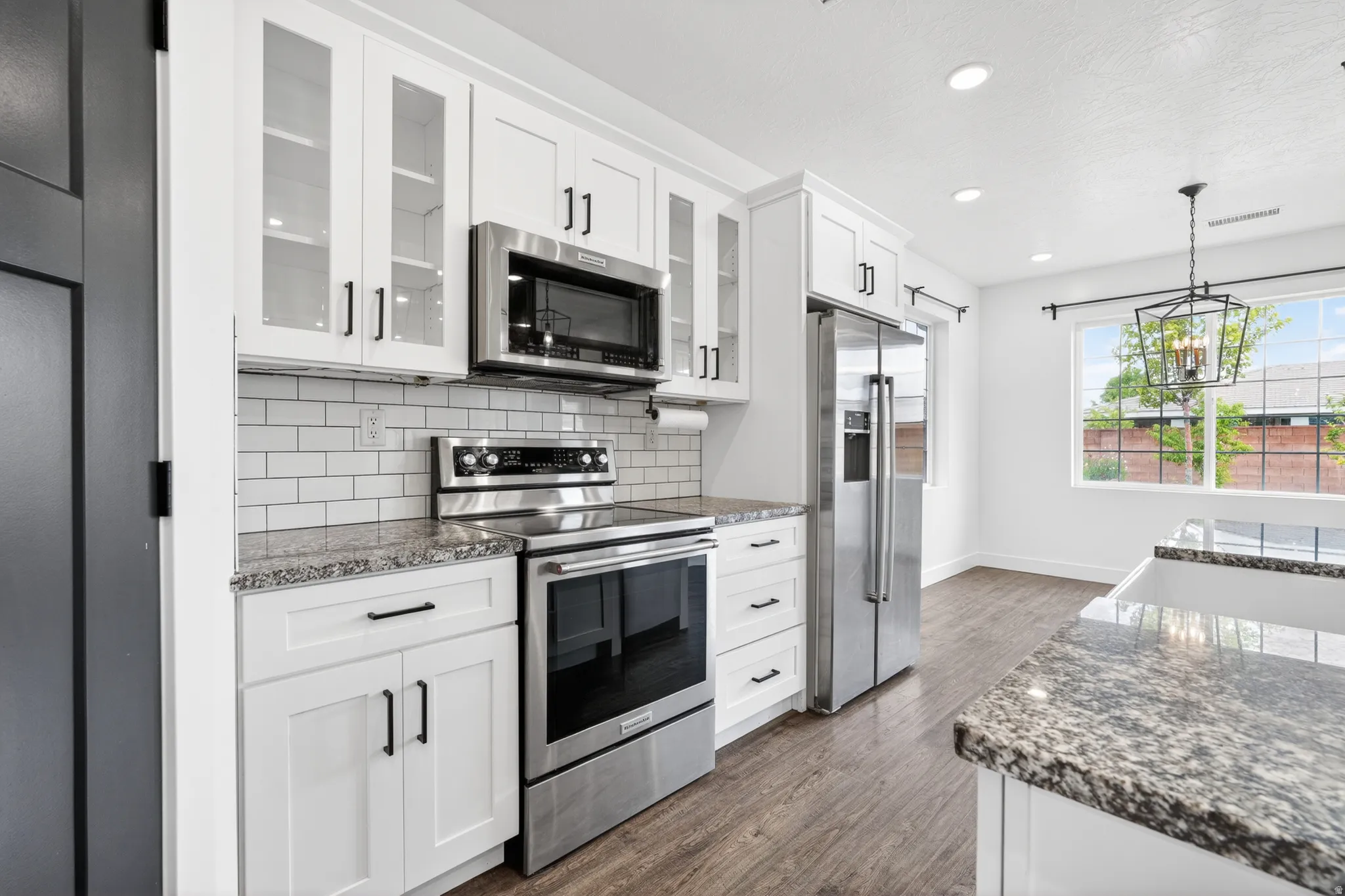 Kitchen with dark stone counters, stainless steel appliances, white cabinets, and dark wood-style flooring