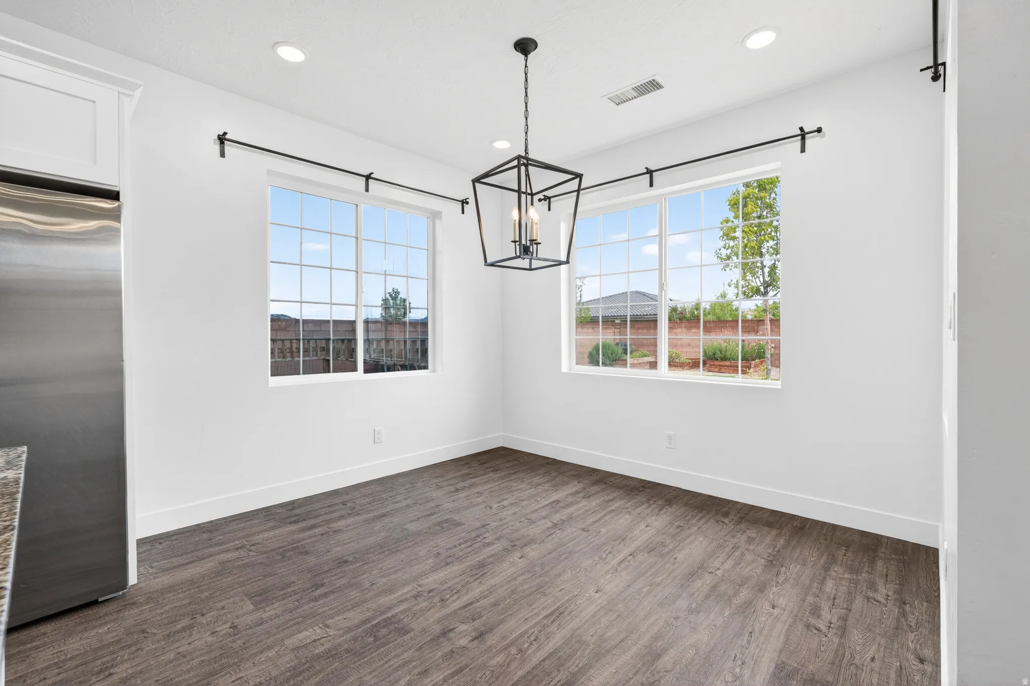 Unfurnished dining area with dark wood-style floors and hanging lights