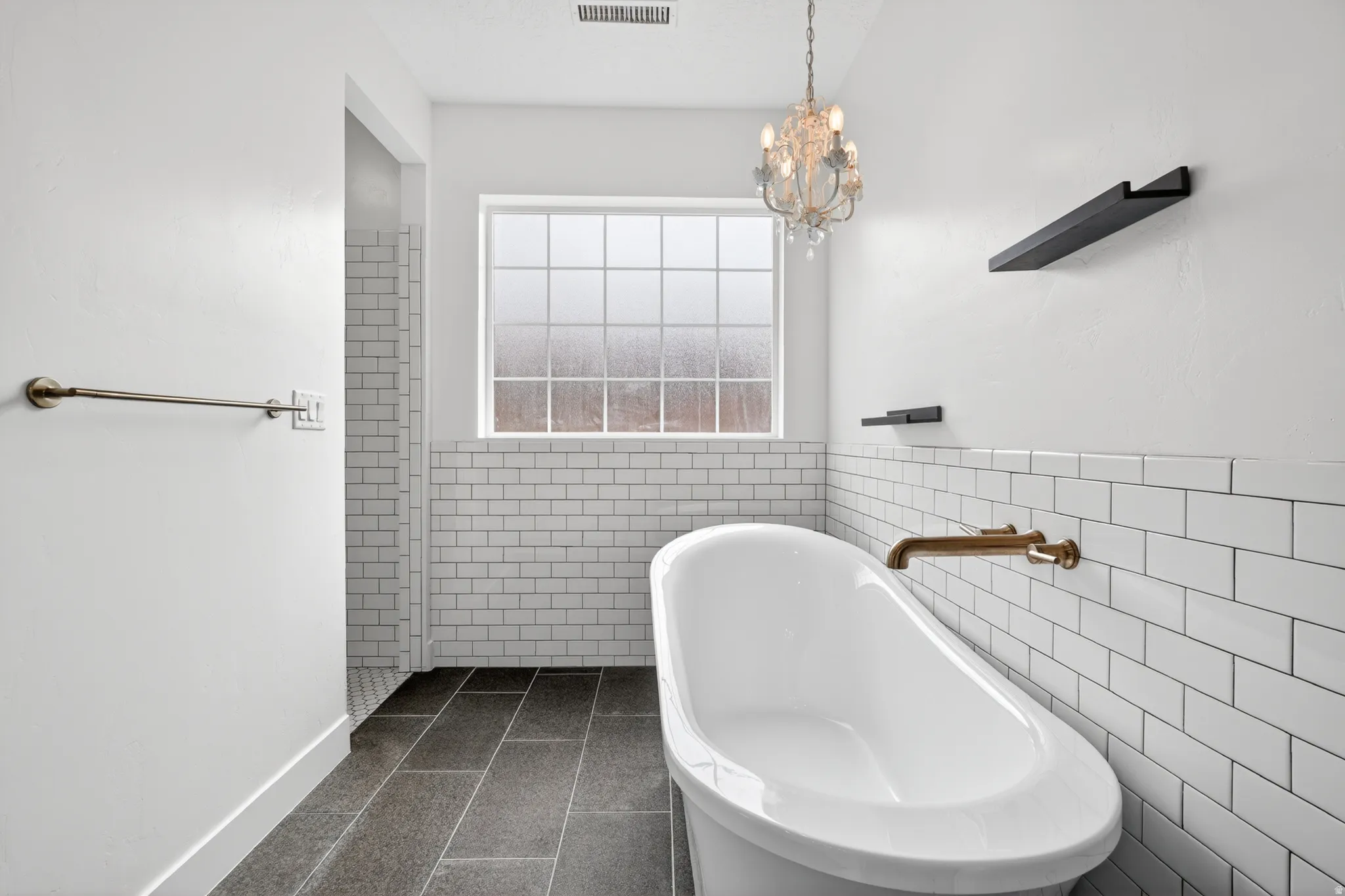 Bathroom with tile walls, dark tile patterned floors, a freestanding bath, a chandelier, and a wainscoted wall