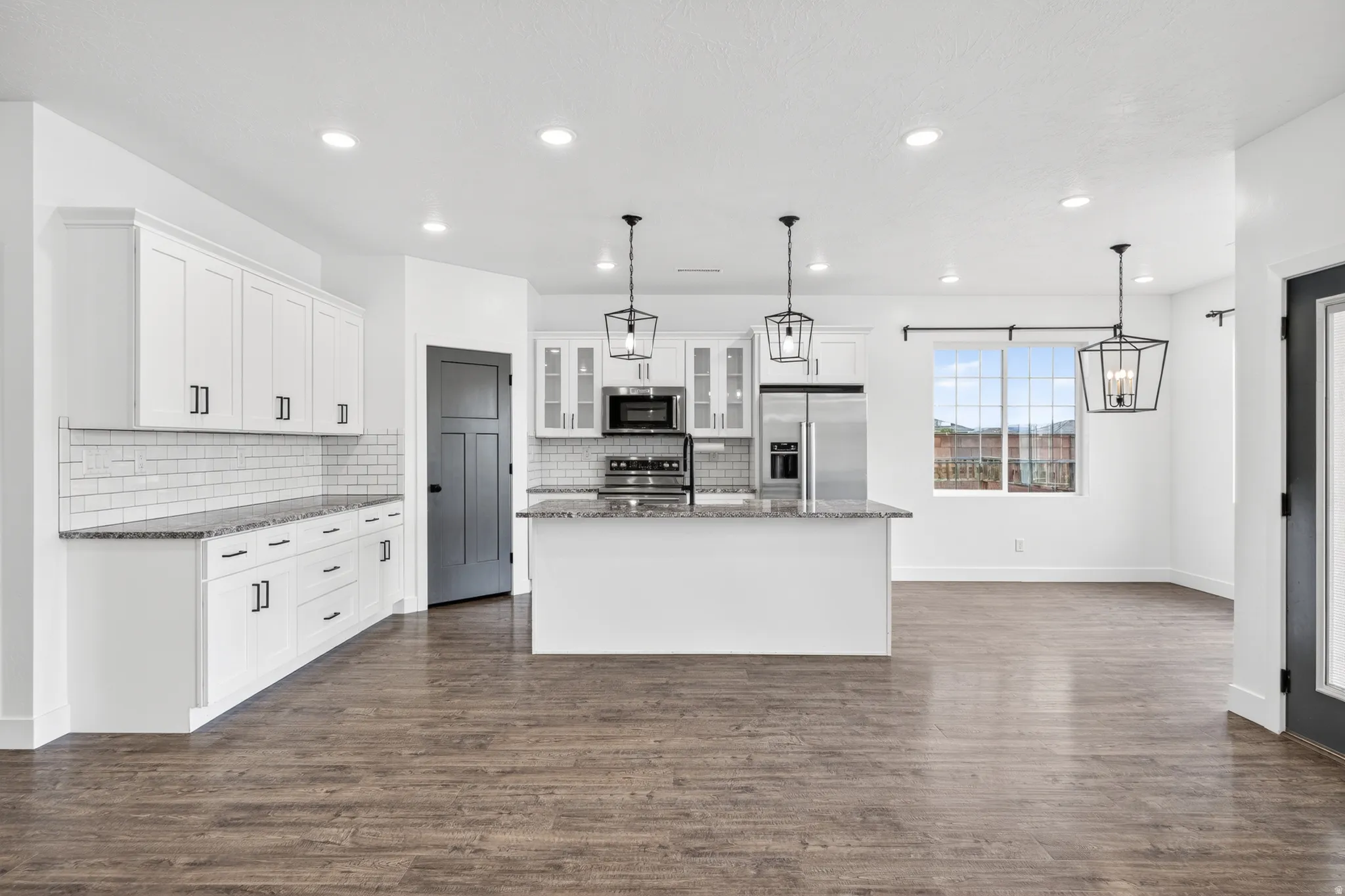 Kitchen featuring dark stone countertops, stainless steel appliances, a kitchen island with sink, and hanging light fixtures