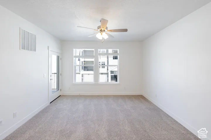 Carpeted room featuring a ceiling fan with integrated lighting, multiple windows, and a glass-paneled door