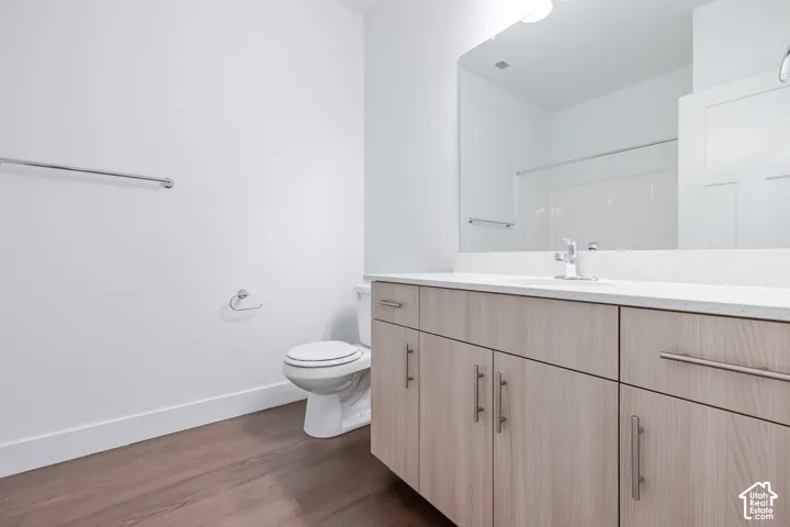 Wood-finish flooring, light wood-tone vanity cabinetry, white countertop, large wall-mounted mirror, and a built-in shower/tub combination