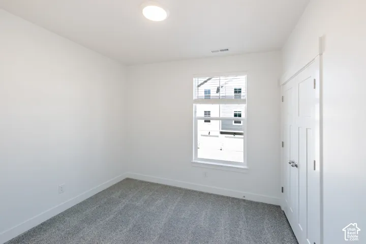 Plush gray carpeting, white walls, double-pane window, and a paneled door with round knob hardware