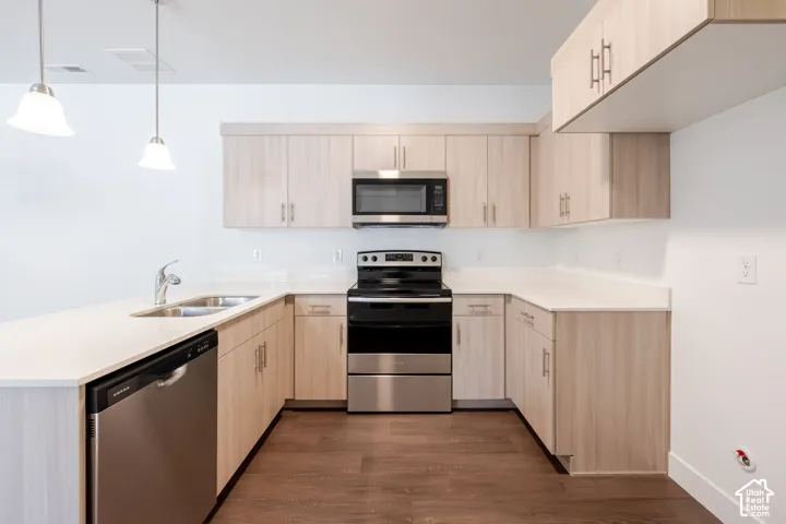 U-shaped kitchen with light wood-finish cabinetry, stainless steel appliances, a double basin sink, and pendant lighting