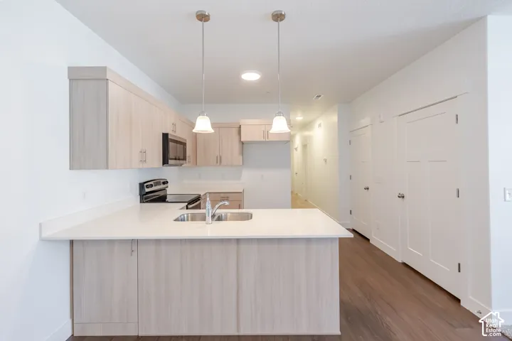 Kitchen featuring light wood-finish cabinetry, stainless steel sink, integrated microwave, and pendant lighting