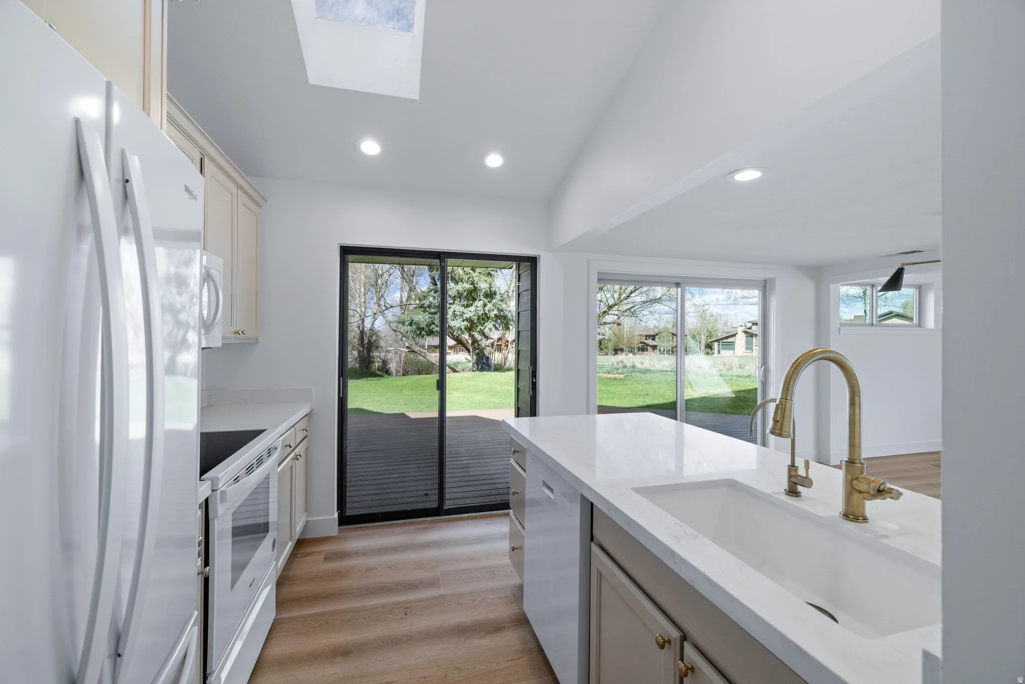 Kitchen with white appliances, lofted ceiling, light wood-style flooring, a skylight, and light stone counters