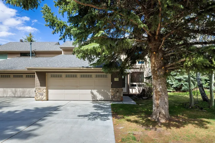 View of front of house featuring roof with shingles, stone siding, driveway, a garage, and a front yard