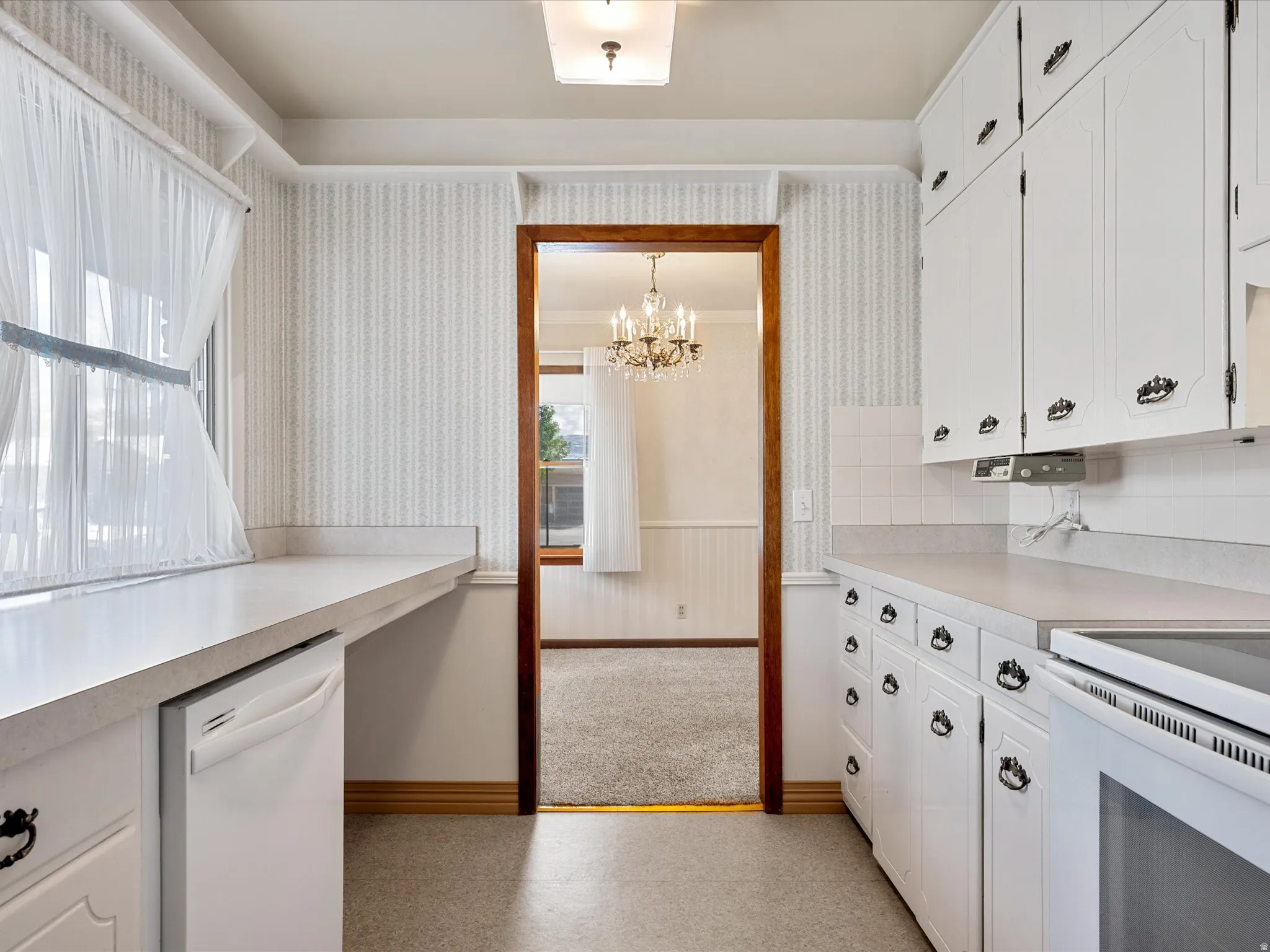 Kitchen with white cabinetry, wainscoting, light countertops,  and white appliances