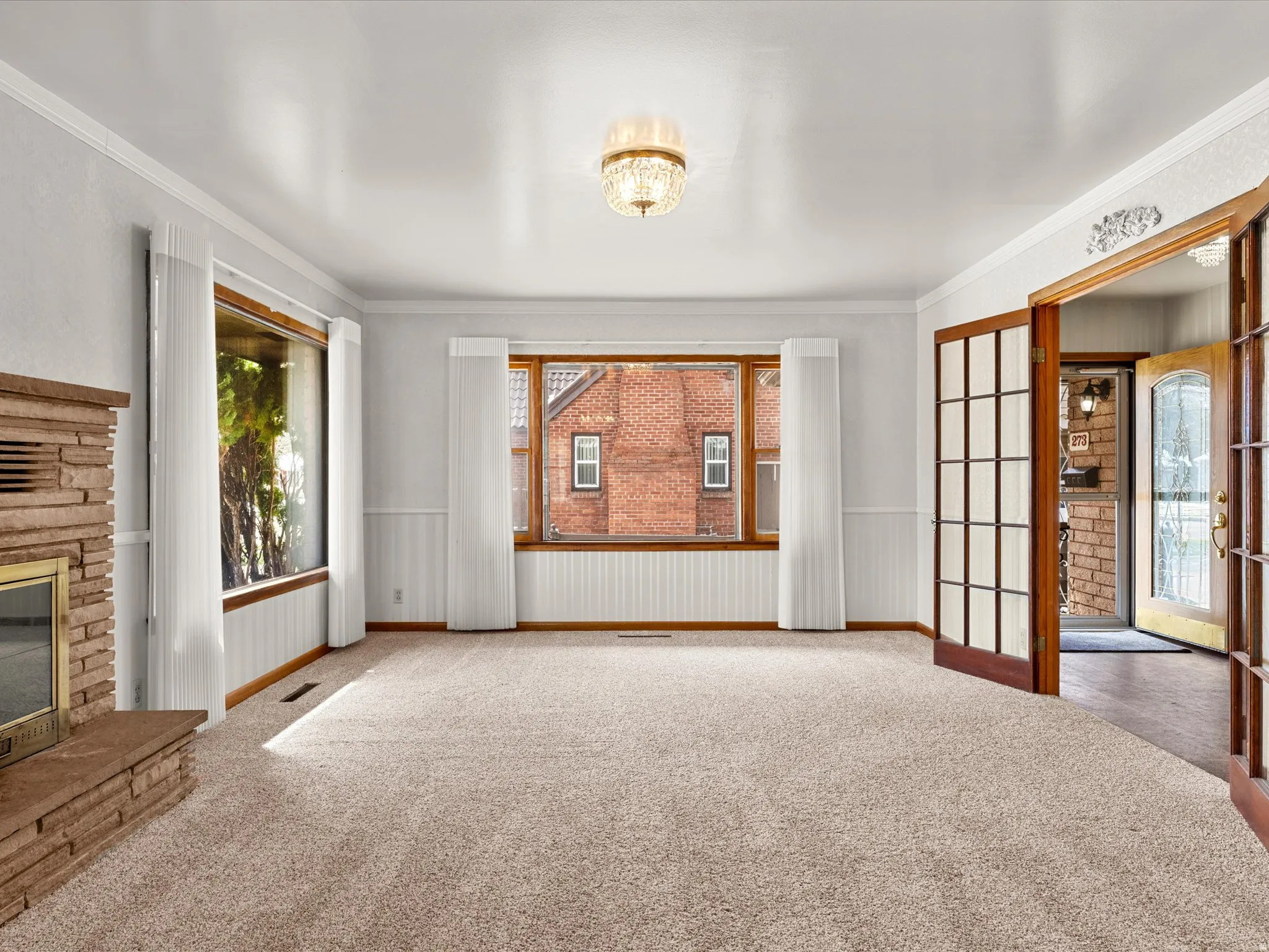 Unfurnished living room with wainscoting, a stone fireplace, carpet flooring, and crown molding