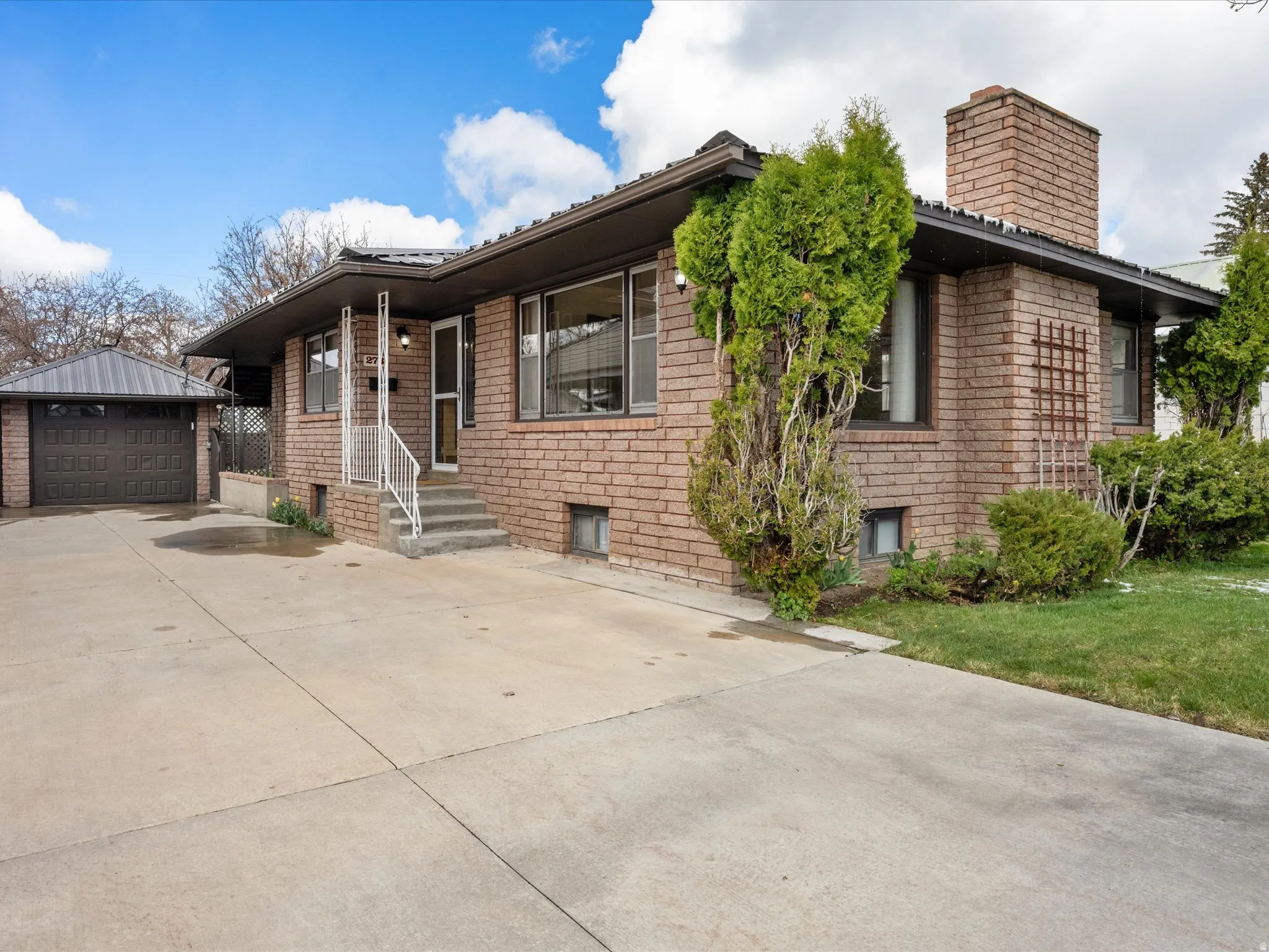 Ranch-style home featuring a chimney, a garage, an outdoor structure, and brick siding
