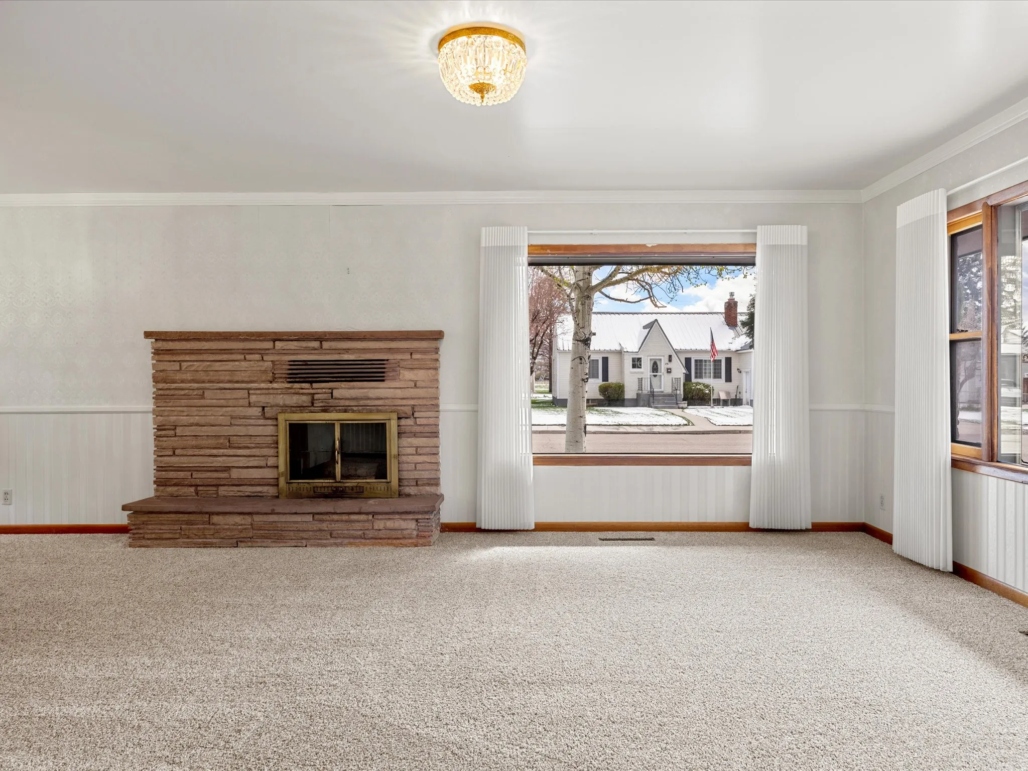 Unfurnished living room with wainscoting, carpet floors, a stone fireplace, and ornamental molding