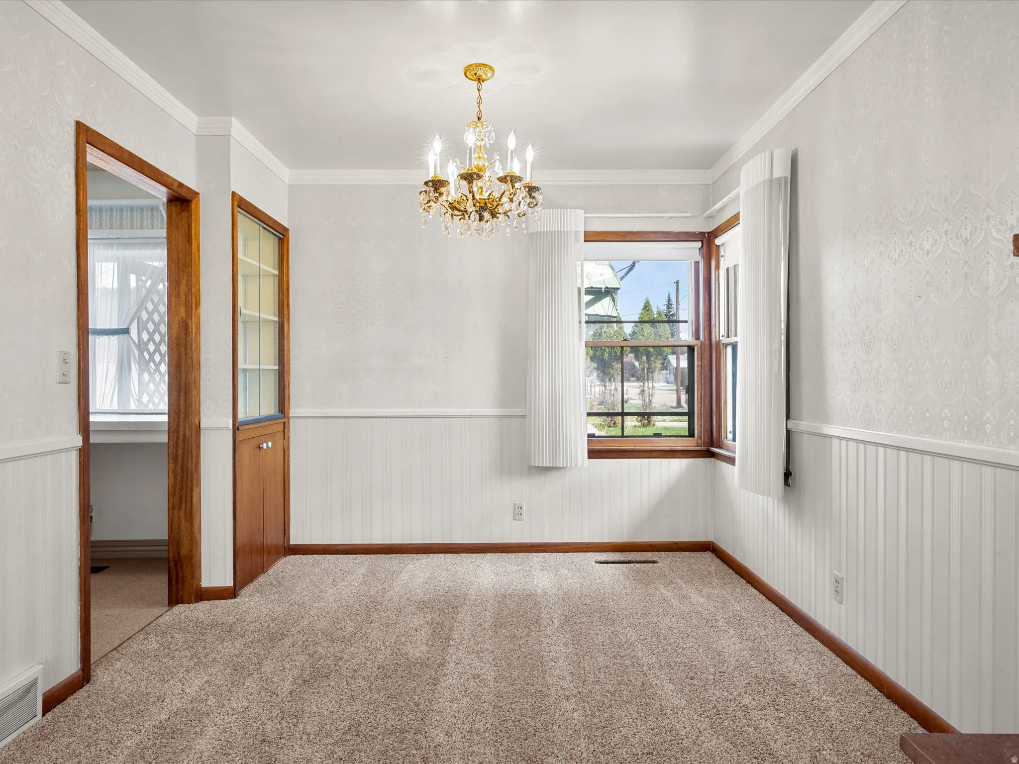 Empty room with hanging lights, a wainscoted wall, carpet floors, and crown molding