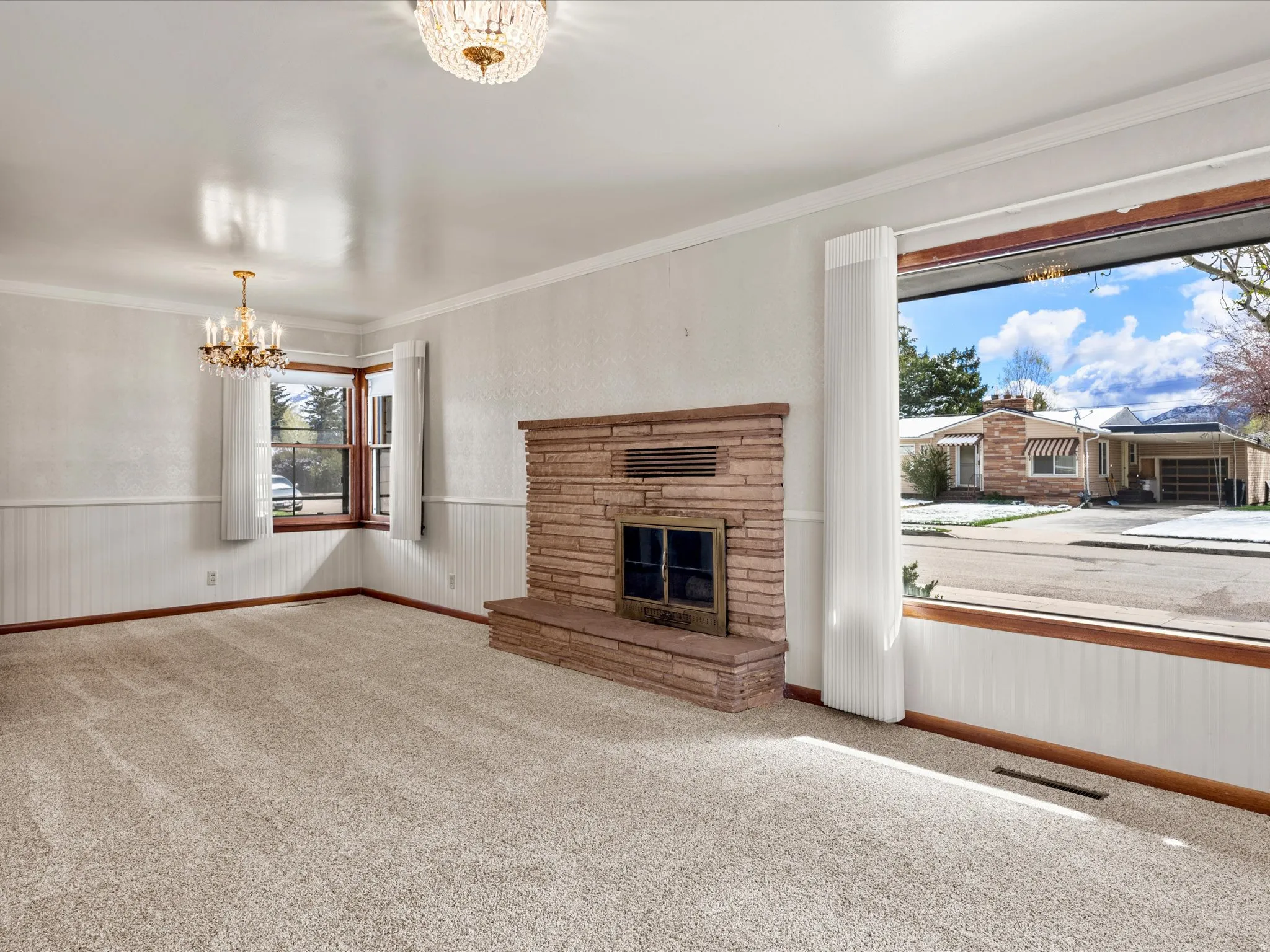 Unfurnished living room with carpet floors, a wainscoted wall, hanging lights, a fireplace, and ornamental molding