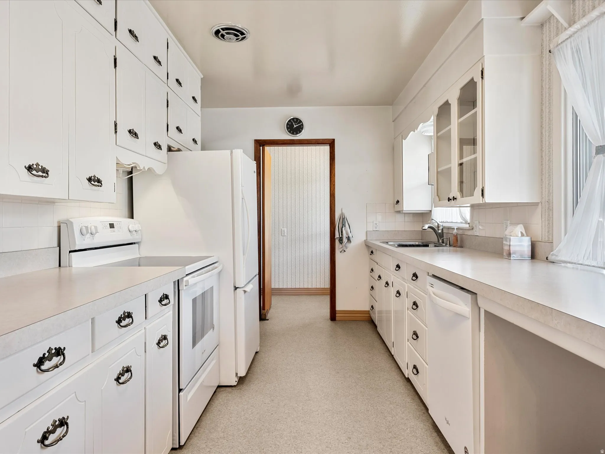 Kitchen featuring white appliances, light countertops, white cabinets, and tasteful backsplash
