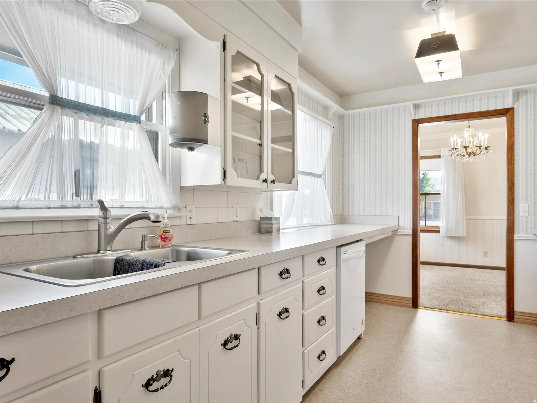 Kitchen with white cabinets, light countertops, suspended lighting, dishwasher