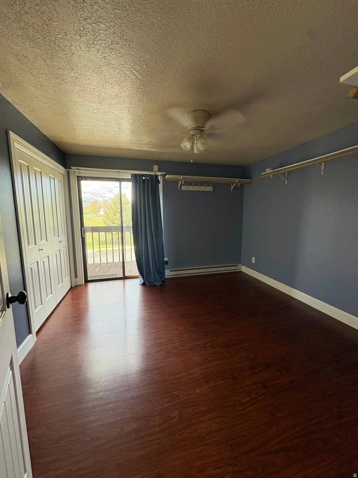 Spacious room featuring wood-finish flooring, a ceiling fan, and sliding glass doors leading to a private balcony