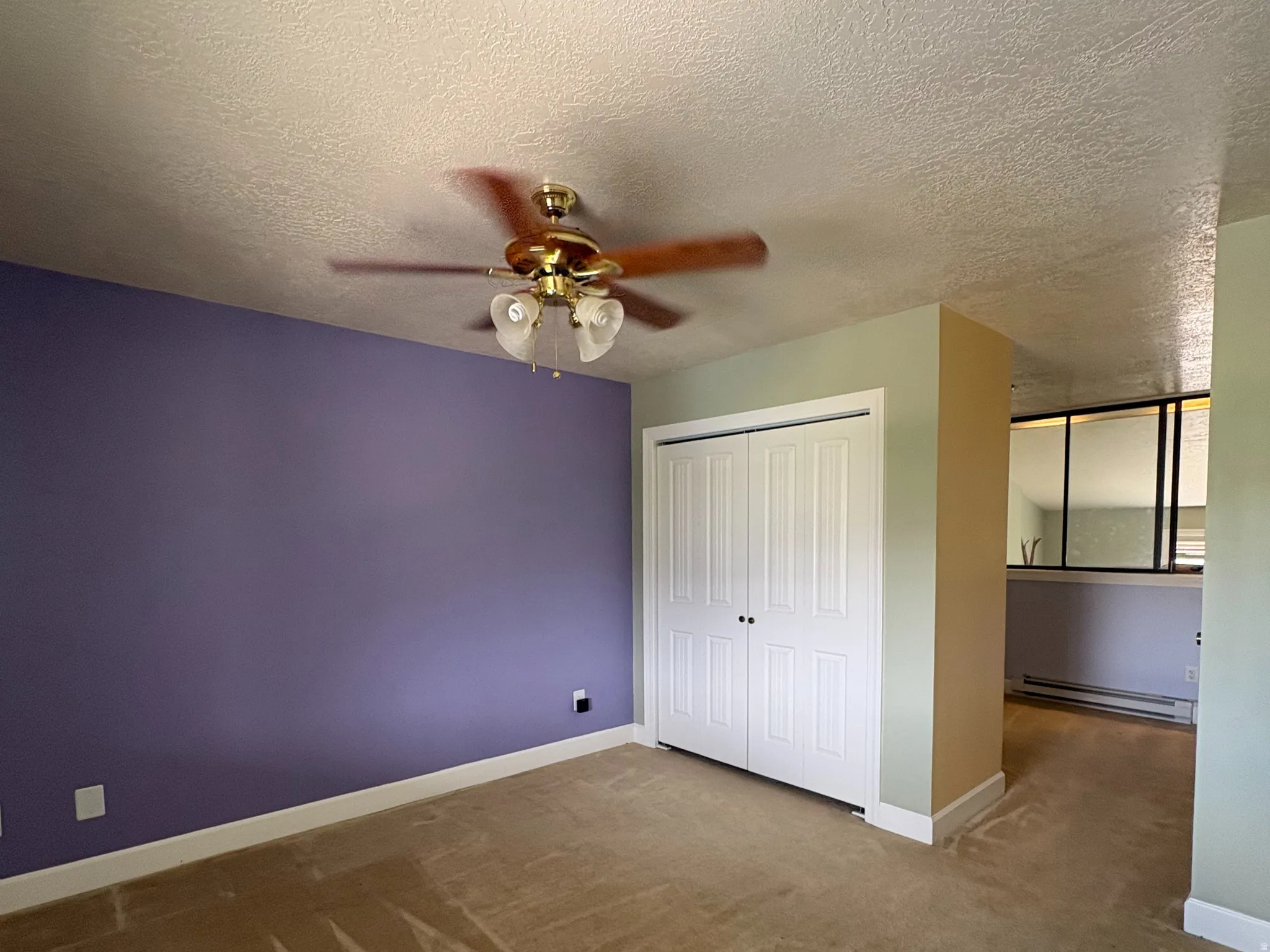 Carpeted interior space featuring a ceiling fan with light fixture, bi-fold closet doors, and contrasting wall colors
