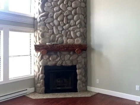 Unfurnished living room featuring a baseboard heating unit, dark wood-style flooring, and a stone fireplace
