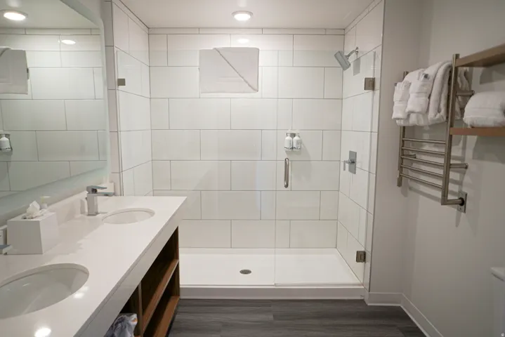 Full bathroom with double vanity, a towel warmer, a stall shower, dark wood-type flooring, and radiator