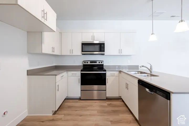 Kitchen featuring extensive white cabinetry, light countertops, stainless steel appliances, and wood-finish flooring