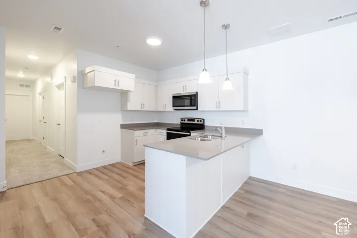 Kitchen featuring white cabinetry, stainless steel appliances, a light-toned countertop, and pendant lighting