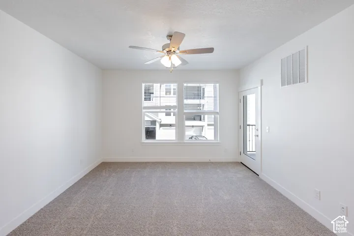 Light-filled room featuring neutral carpeting, a ceiling fan with integrated lighting, a large window, and a glass-paneled door