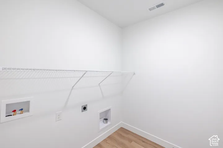 Laundry area featuring wood-finish flooring, white walls, and a wire shelf