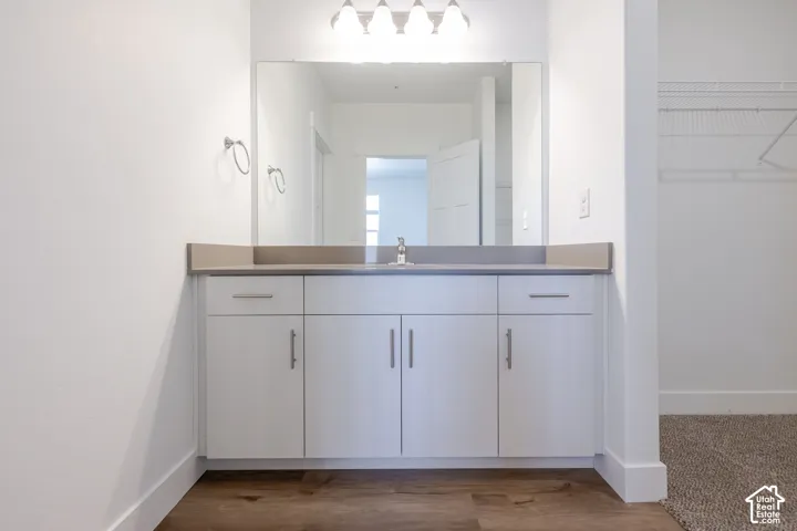 White vanity with brushed nickel hardware, light-toned countertop, large mirror, and wood-finish flooring