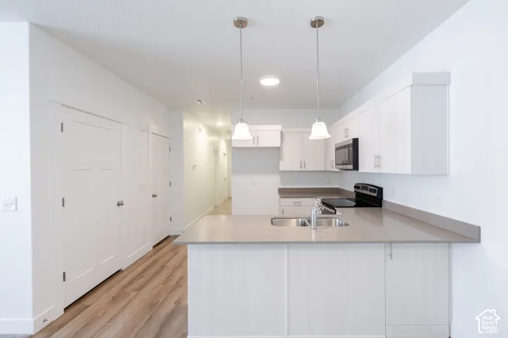 Kitchen island with an undermount sink, pendant lighting, built-in microwave, and wood-finish flooring