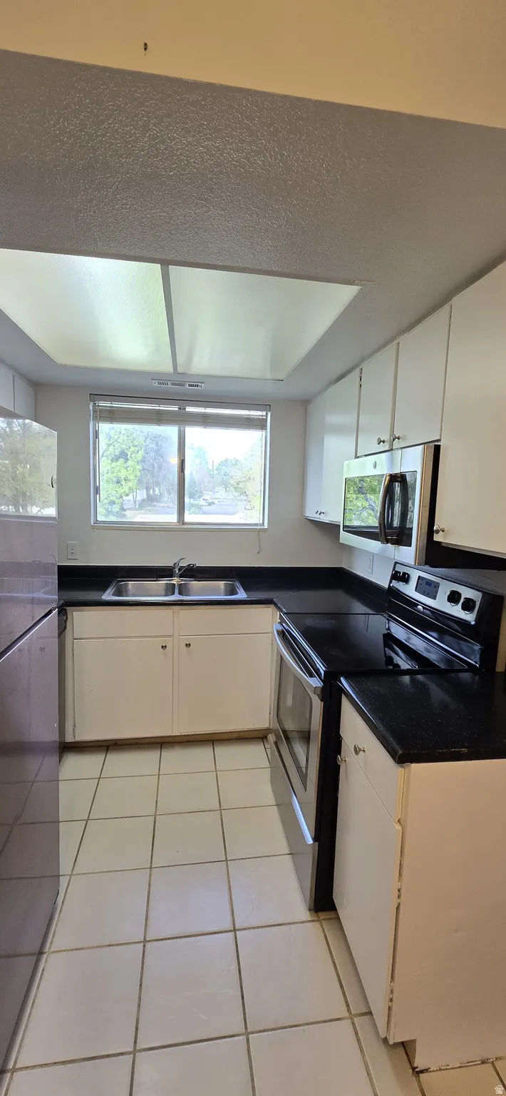 Kitchen featuring stainless steel appliances, light tile patterned floors, white cabinetry, and plenty of natural light