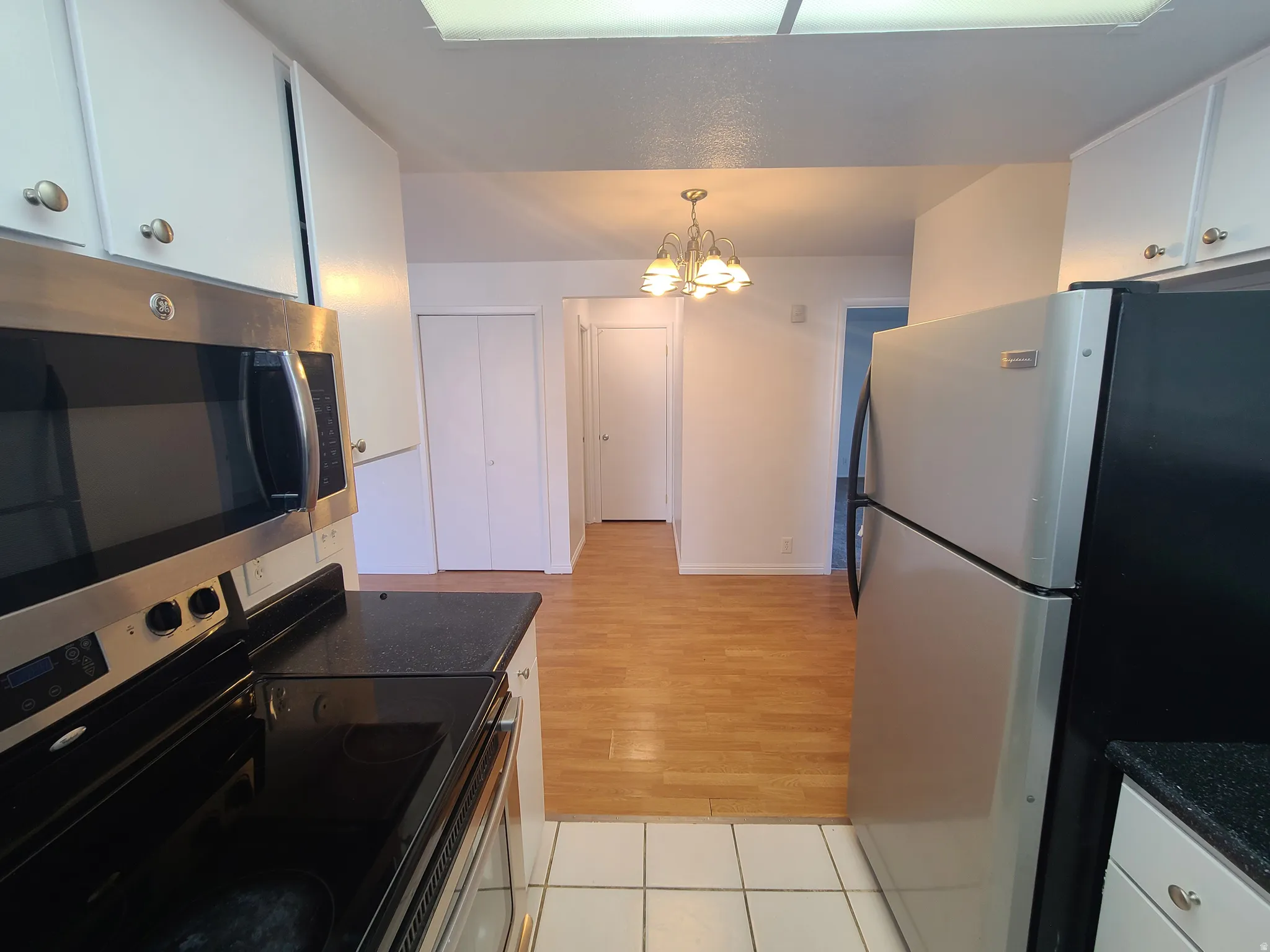 Kitchen featuring stainless steel appliances, white cabinets, hanging lights, and dark countertops