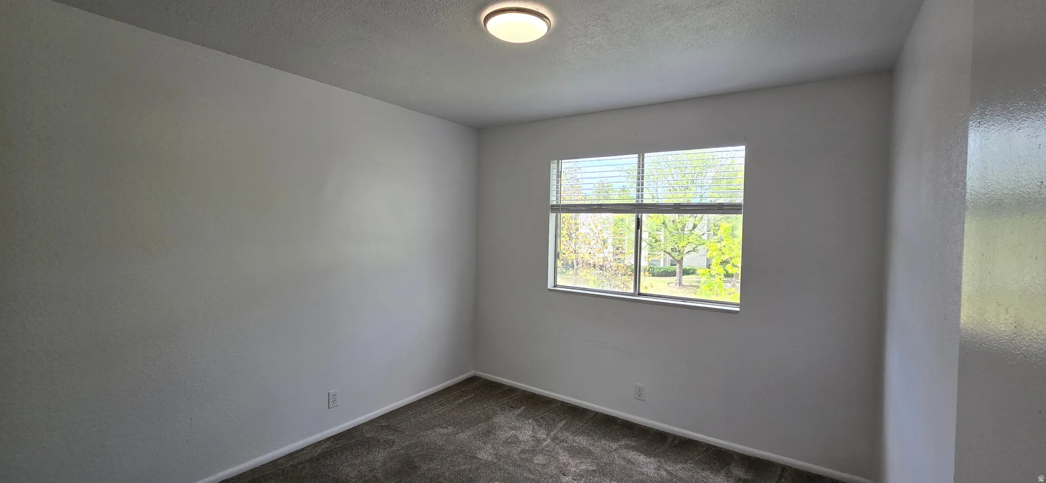 Spare room featuring dark colored carpet, a textured ceiling, and a textured wall