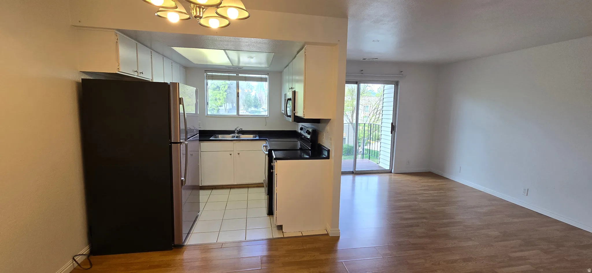 Kitchen with freestanding refrigerator, dark countertops, black range with electric stovetop, suspended lighting, and light wood finished floors