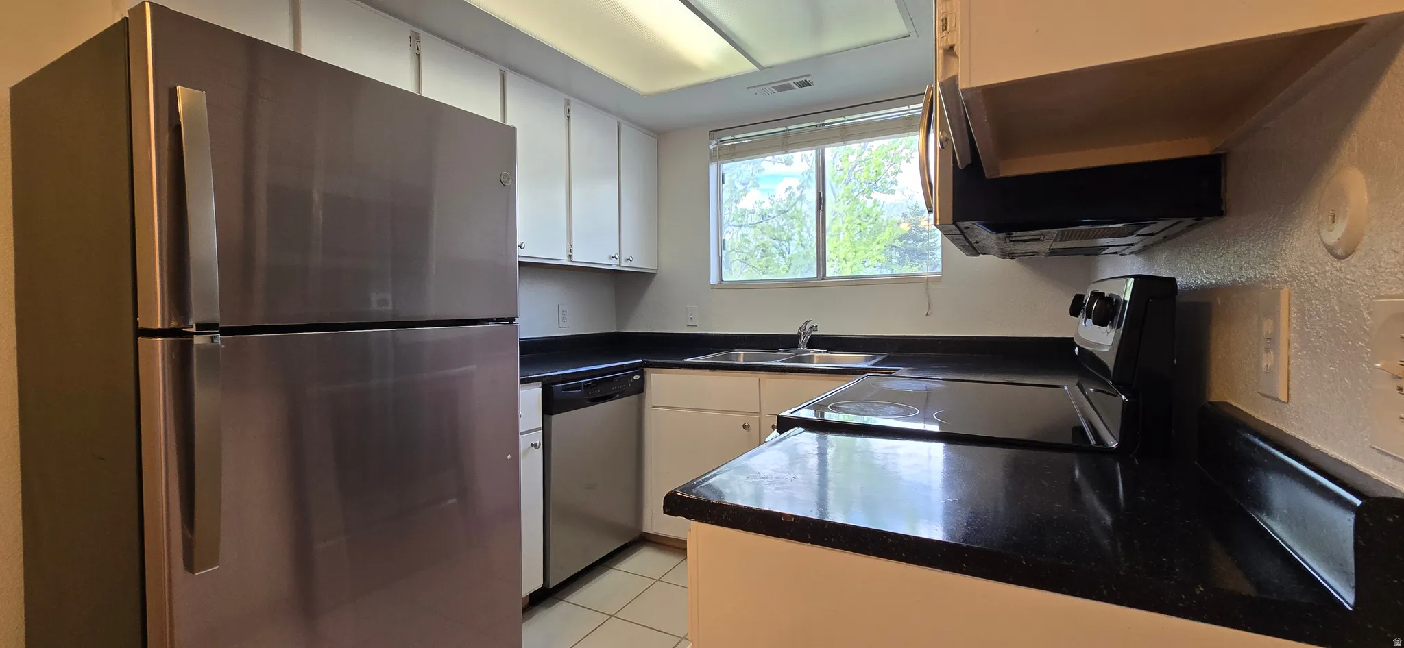 Kitchen with dark countertops, stainless steel appliances, light tile patterned floors, white cabinetry, and a textured wall