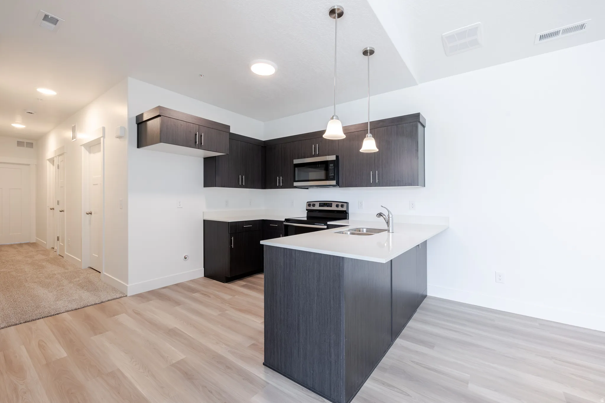 Kitchen featuring wood-finish flooring, dark wood-finish cabinetry, stainless steel appliances, white countertops, and pendant lighting
