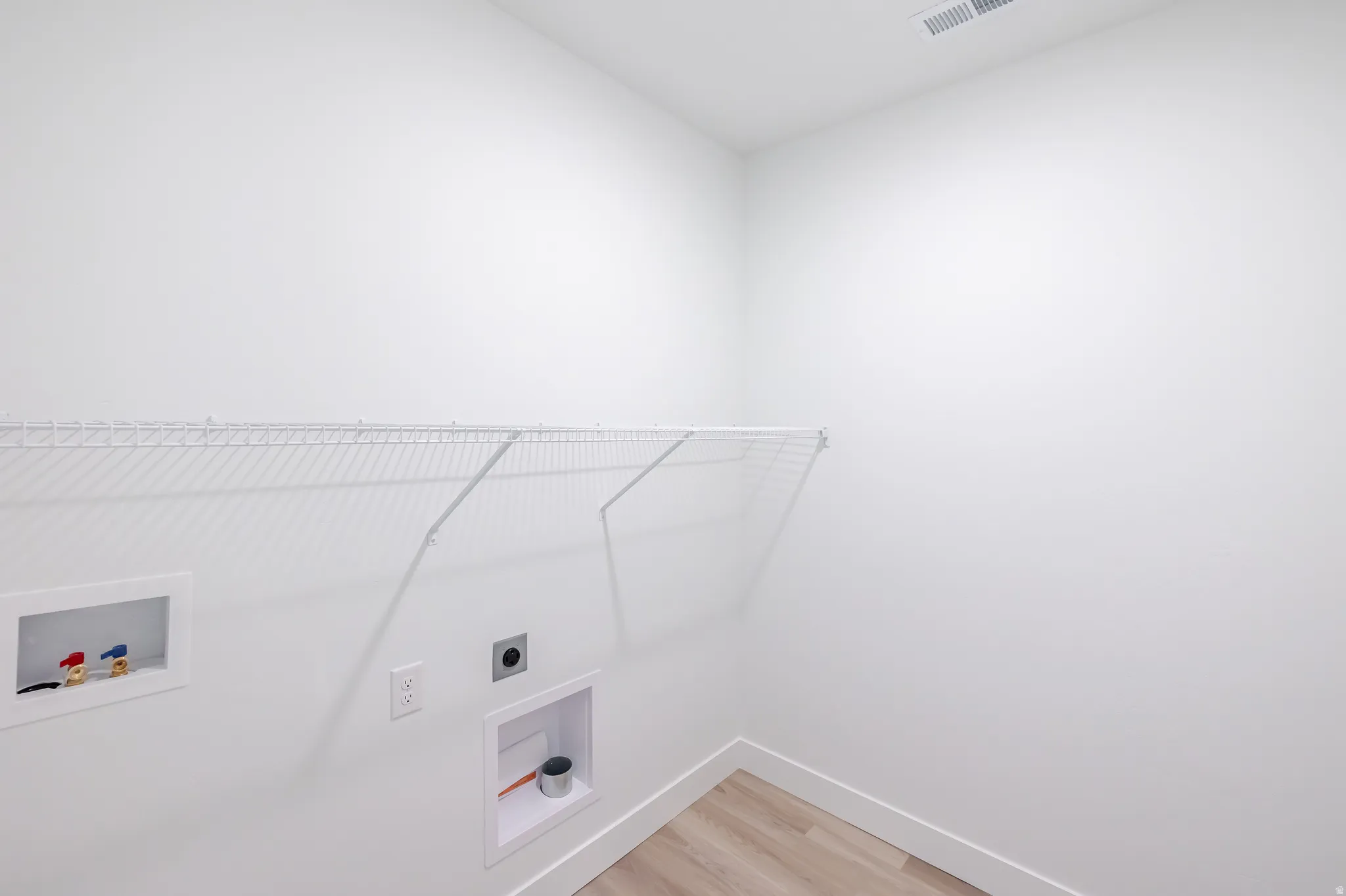 Dedicated laundry area with light wood-finish flooring and a white wire shelf