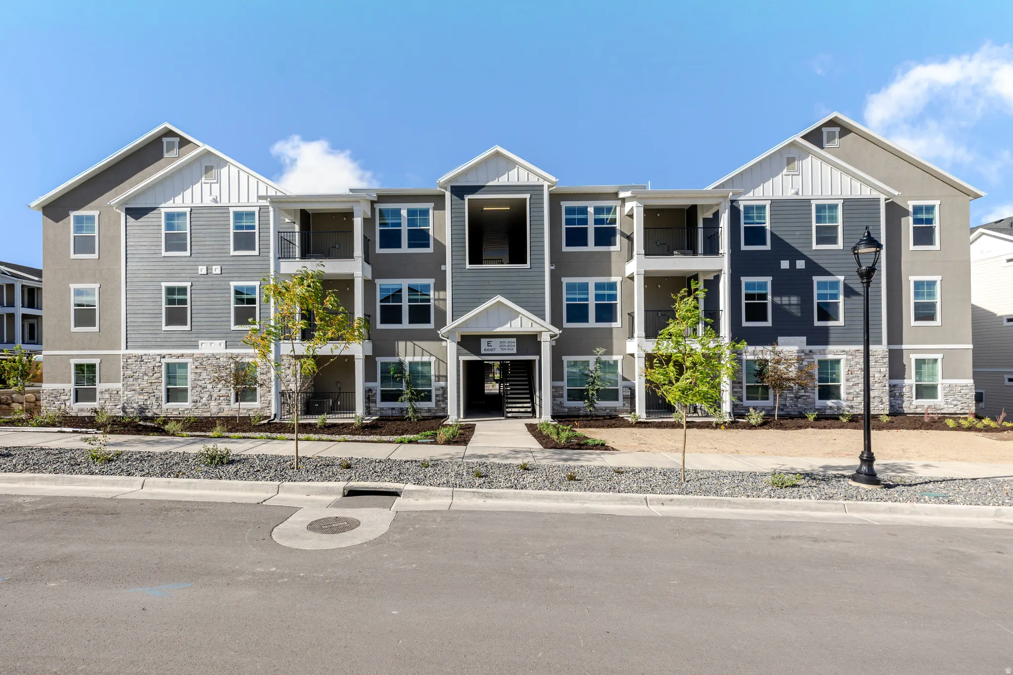 Multi-story building featuring gray horizontal siding, white vertical siding accents, and a stone facade