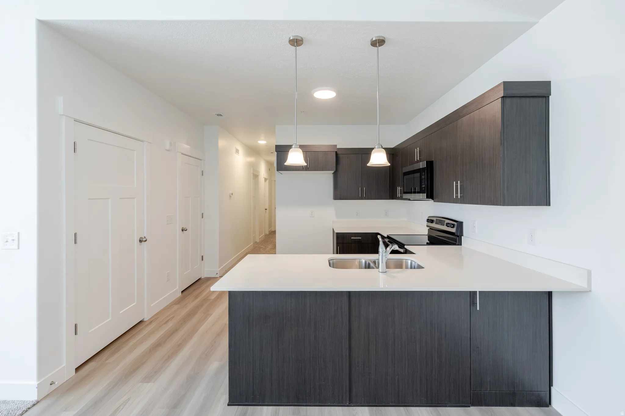 Kitchen featuring dark wood-finish cabinetry, light countertops, and a stainless steel sink with a gooseneck faucet