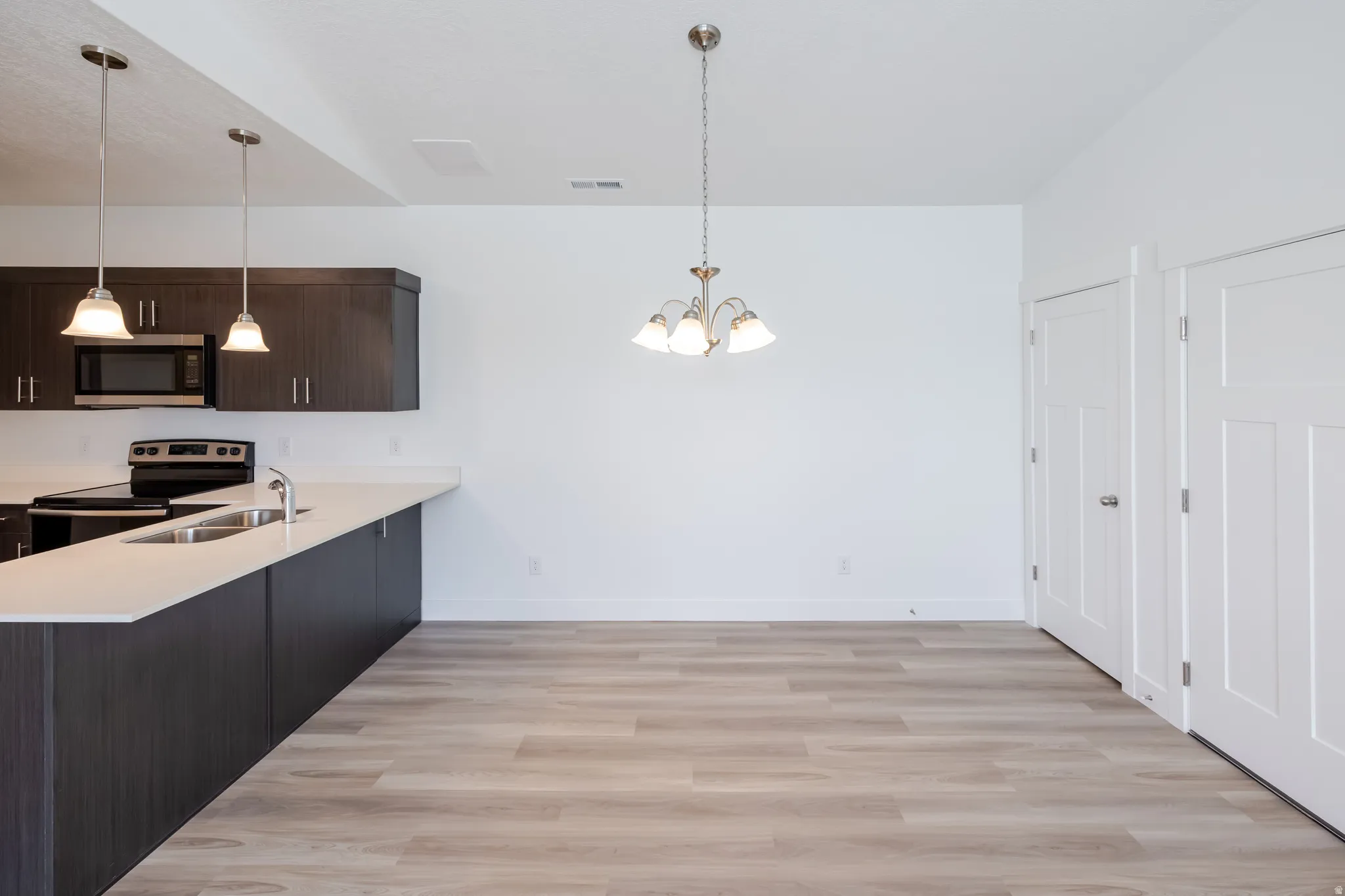 Kitchen and dining area featuring wood-finish flooring, dark wood cabinetry, white countertops, and stainless steel appliances