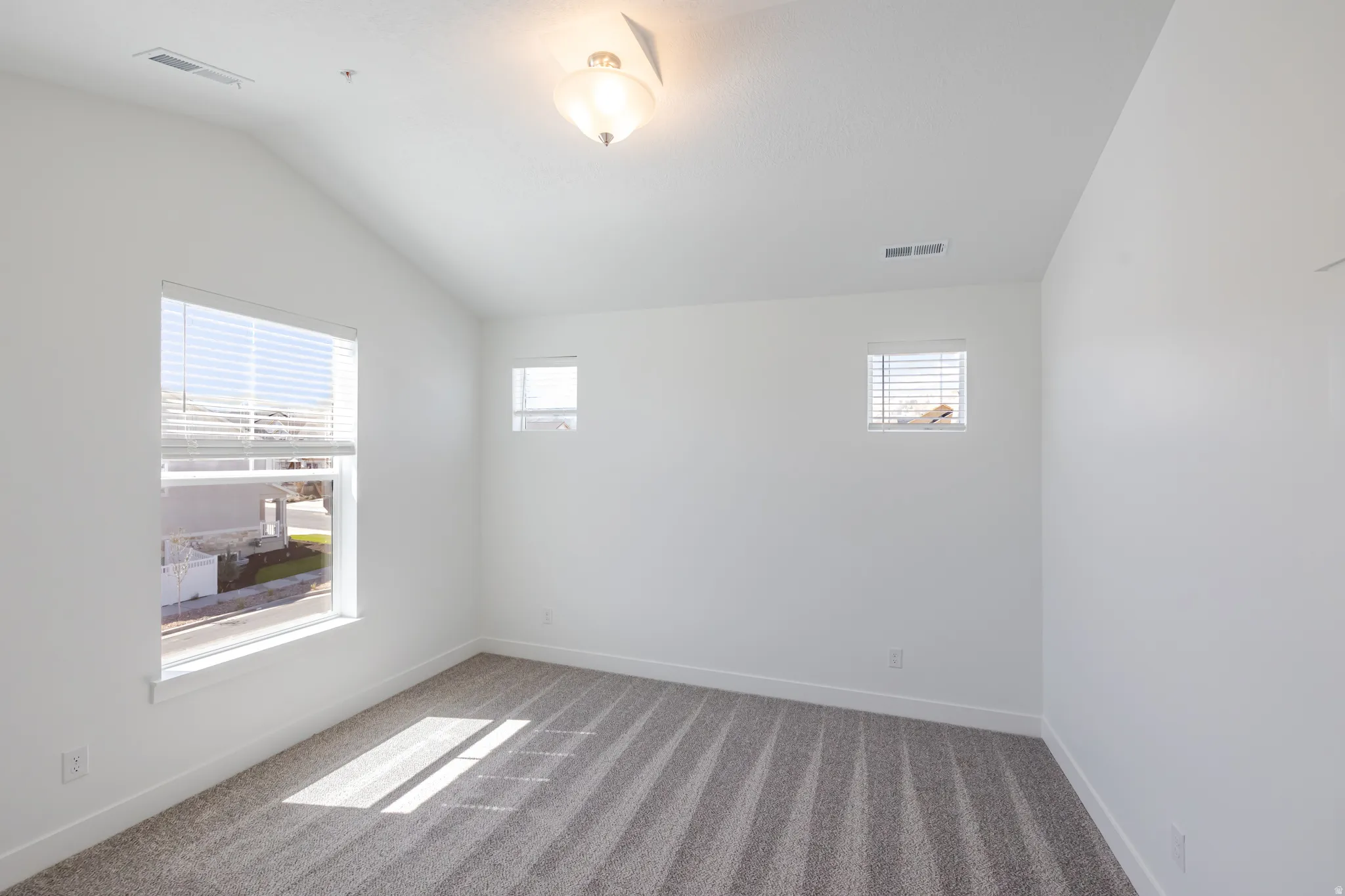 Vaulted ceiling with a flush-mount light fixture, white walls, gray carpet, and multiple windows with blinds