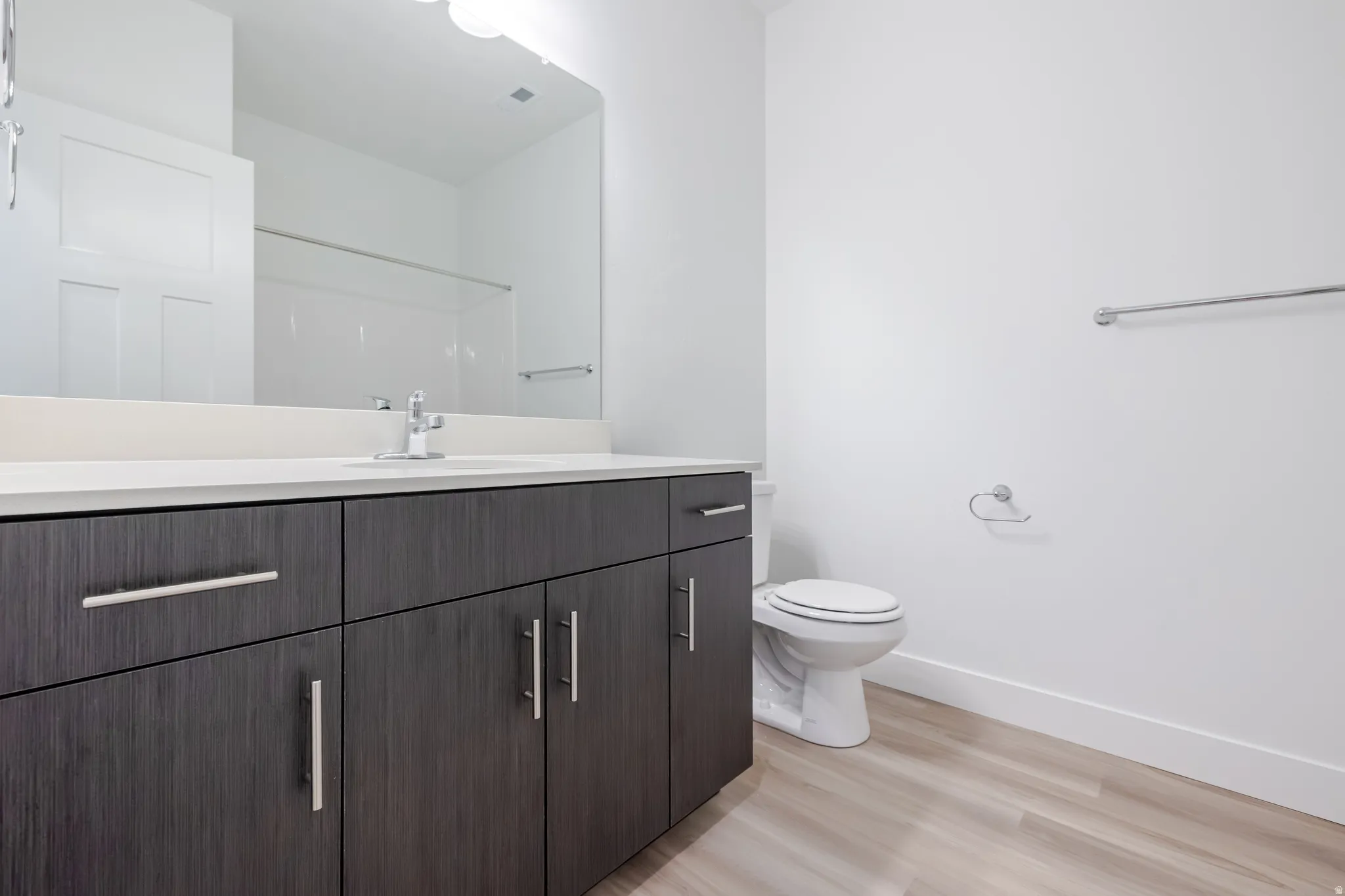 Modern bathroom with a spacious vanity, light-toned wood-finish flooring, and a white countertop