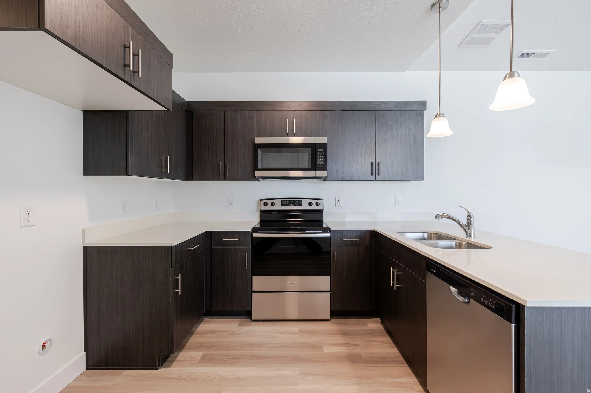 Kitchen with dark wood-finish cabinetry, light countertops, stainless steel appliances, and wood-finish flooring