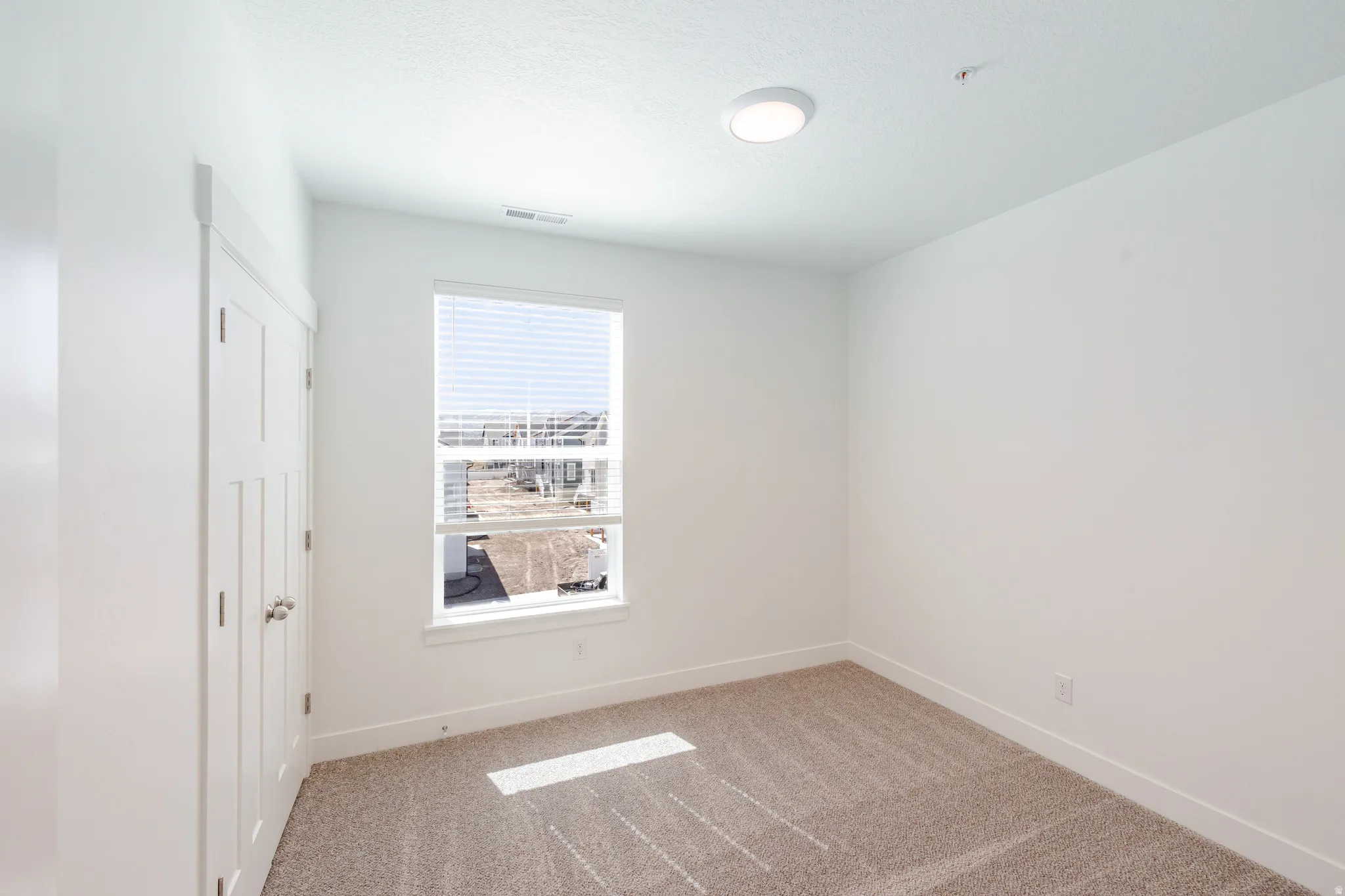 Neutral wall tones, recessed lighting fixture, large window with blinds, white trim, and light-toned carpeting