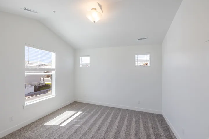 Vaulted ceiling with a flush-mount light fixture, white walls, gray carpet, and multiple windows with blinds