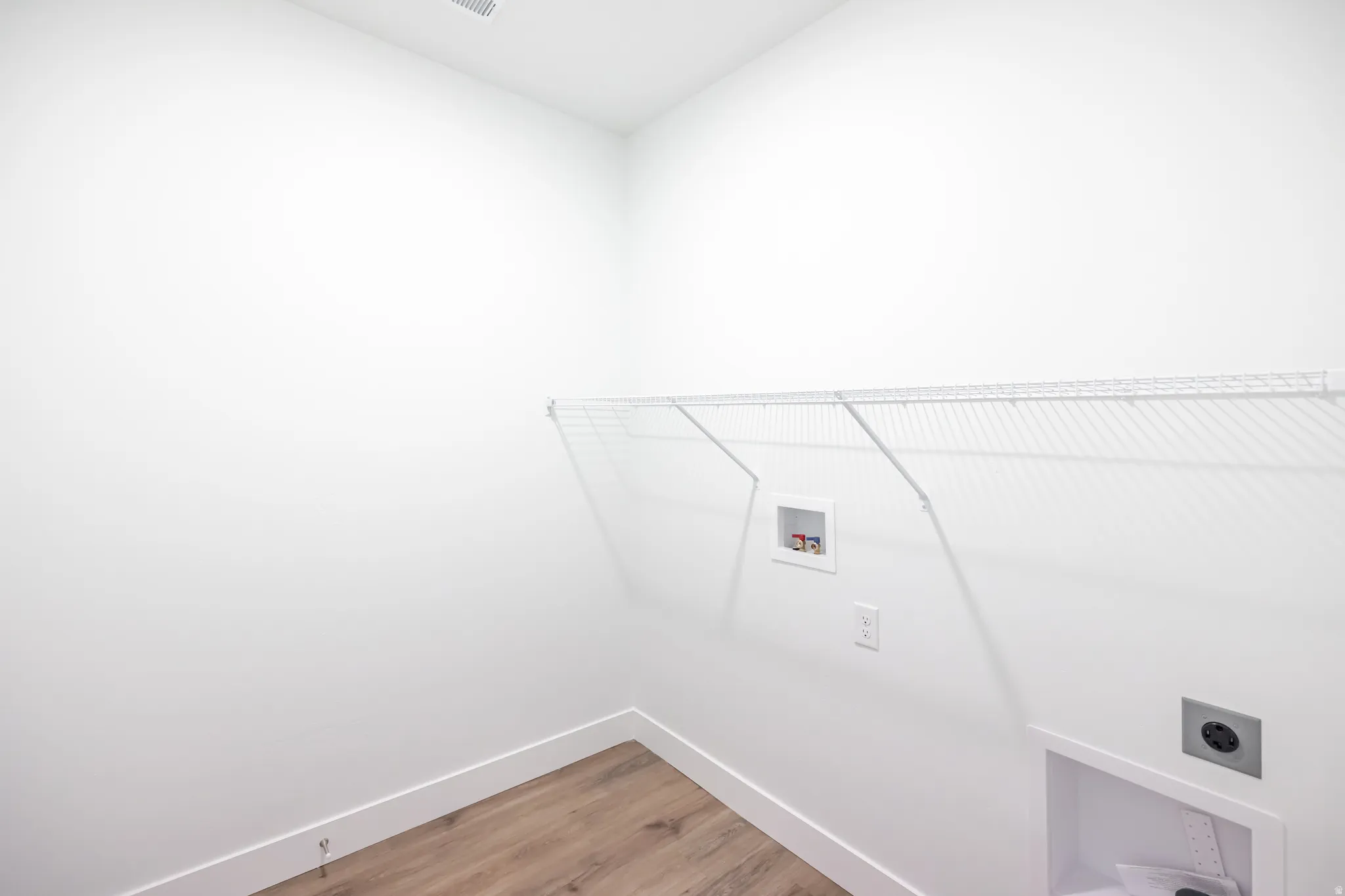 Dedicated laundry area featuring a wire shelf, wall connections, and wood-finish flooring