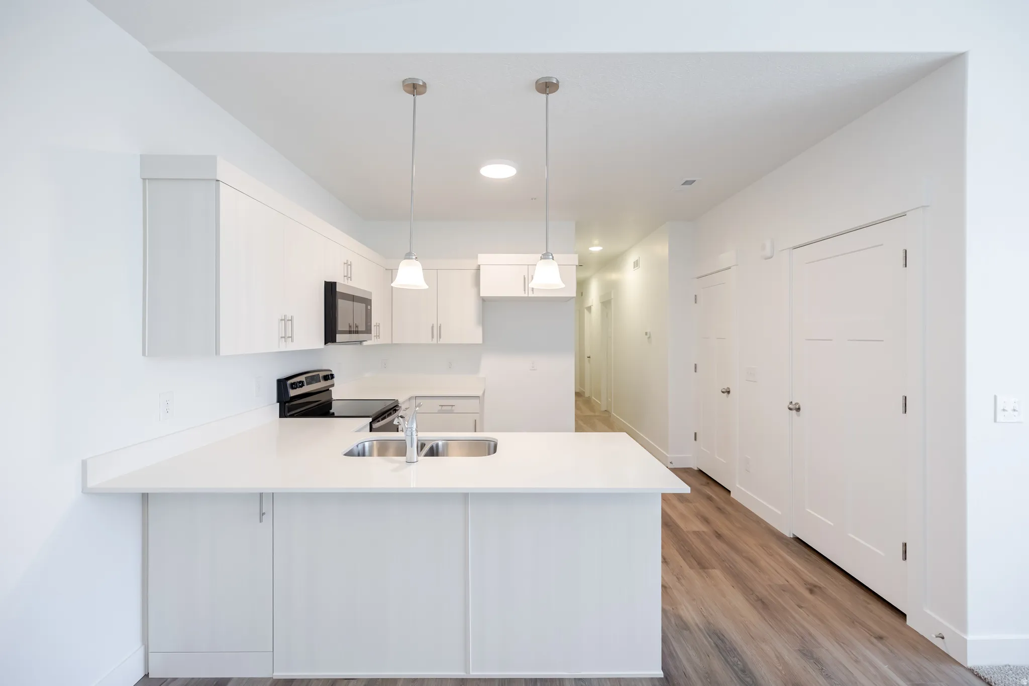 Contemporary kitchen featuring white cabinetry, integrated stainless steel sink, sleek countertops, and pendant lighting