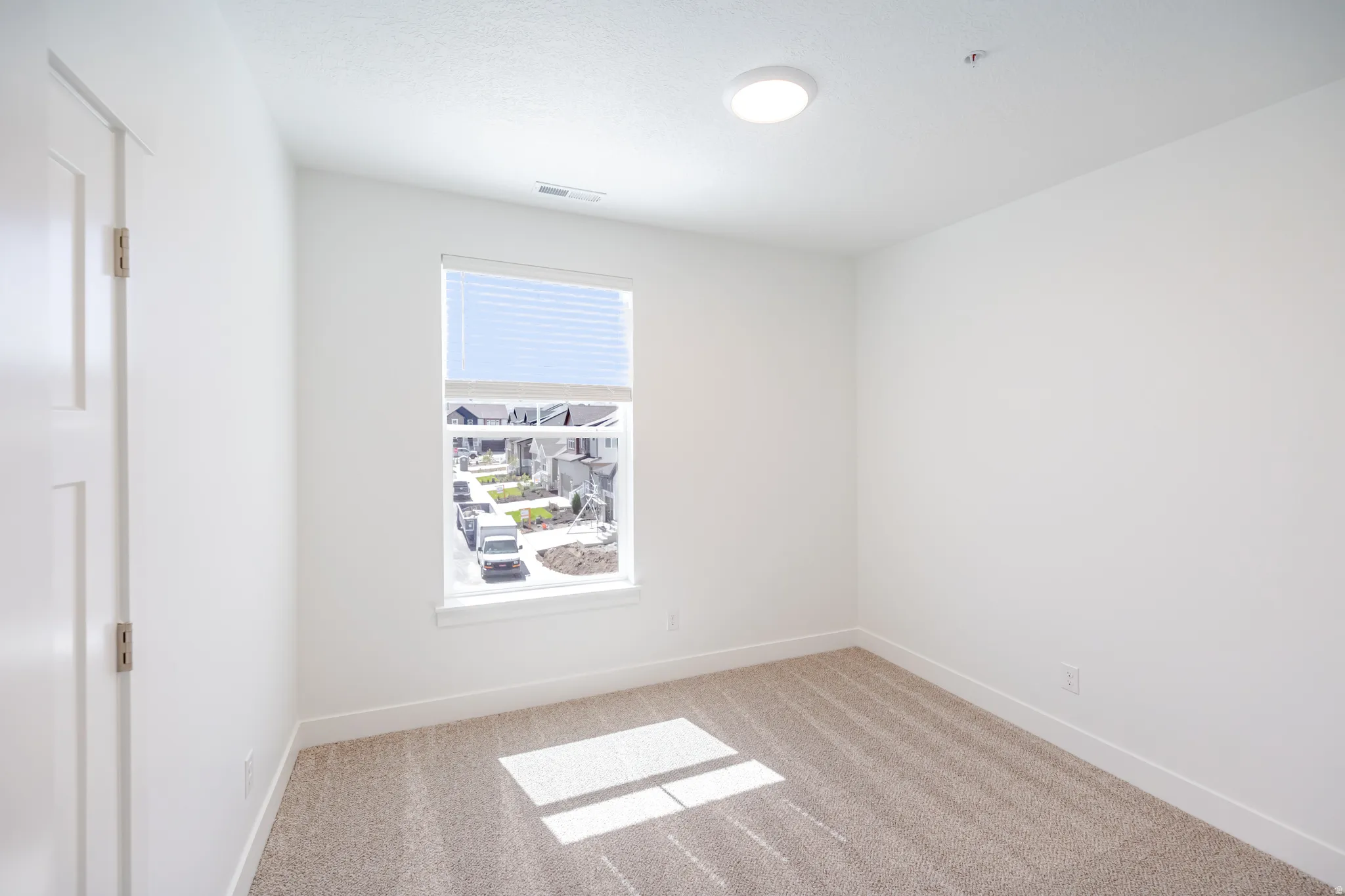 Neutral tone wall paint, textured carpet, window with blinds, flush mount ceiling light, and interior paneled door
